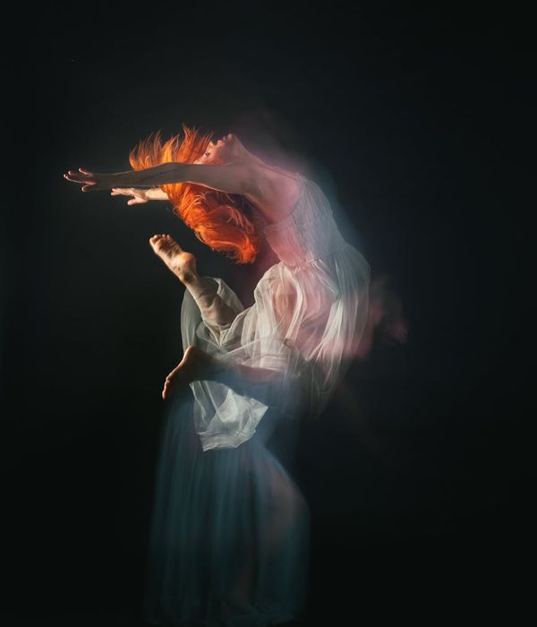 Woman performing a fluid yoga pose against a dark background with green light trails.